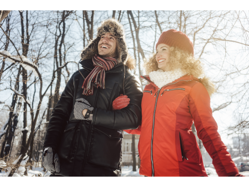 Man and woman walking outside in the cold weather arm in arm wearing winter coats, gloves, and winter hats