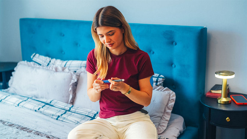 Young woman looking over a GLP-1 injection while sitting on bed at home.