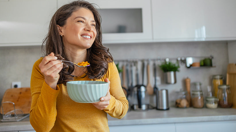 Woman happily eating a bowl of healthy food in her kitchen