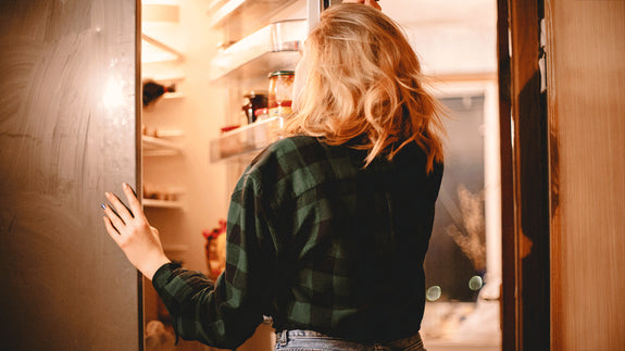 woman standing by an open refrigerator wondering what to eat