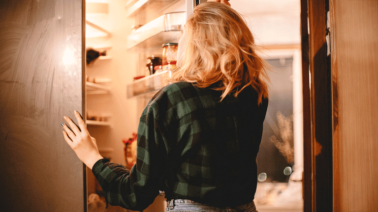 woman standing by an open refrigerator wondering what to eat