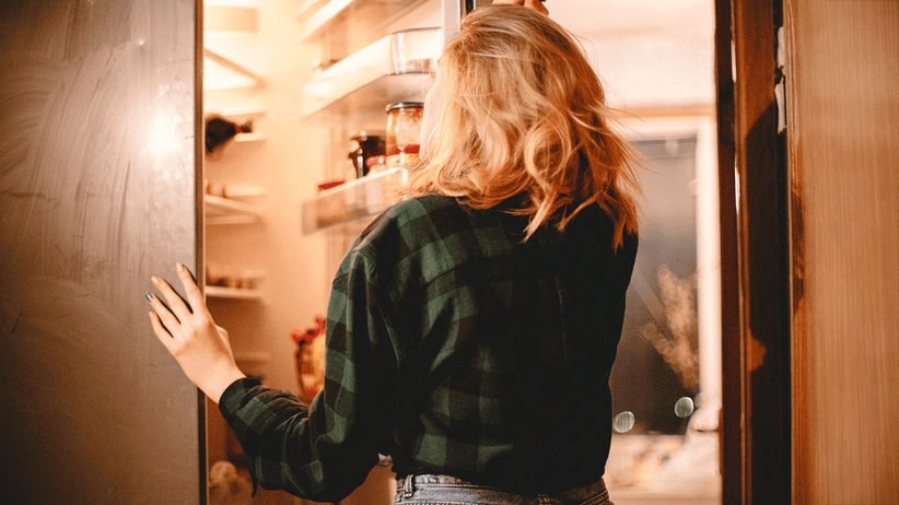 woman standing by an open refrigerator wondering what to eat