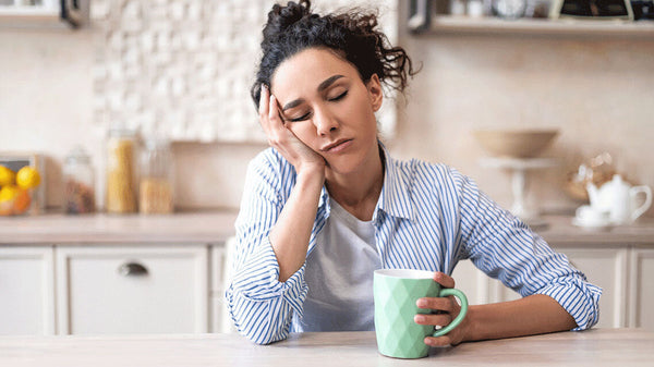Woman sitting at a table looking tired with a cup of coffee in her hand
