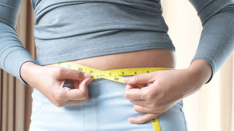 Person holding a measuring tape around her waist to measure it. 
