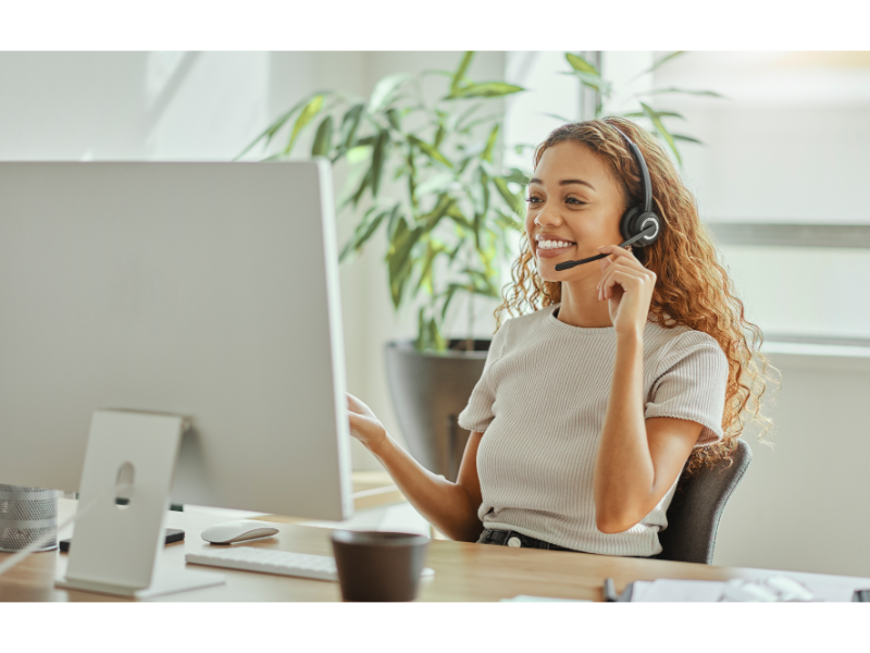 Happy customer service woman sitting at a computer talking on a headset helping a customer.