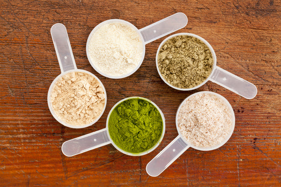 five plastic measuring cups of different  protein powders