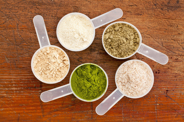 five plastic measuring cups of different  protein powders