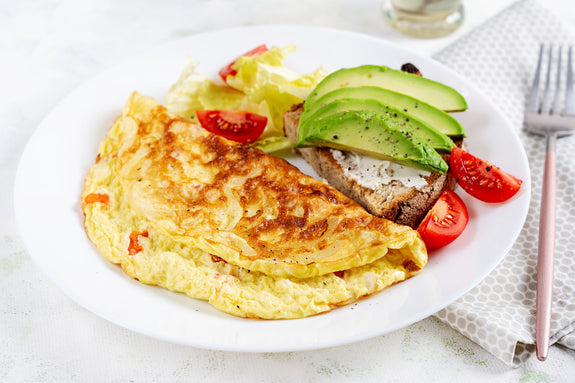 Omelette with tomatoes and toast with avocado on white plate.