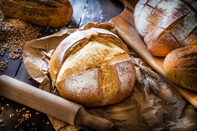 Different types of bread shot on rustic wooden table. A fresh baked loaf of bread is on foreground on a brown craft paper.