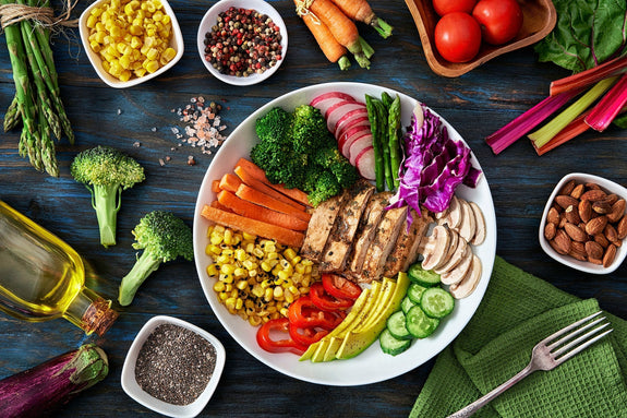 Colorful spring salad on rustic white wood table. Included ingredients: Chicken, tomatoes, broccoli, lettuce, bell peppers, mushroom, carrots, radicchio, almonds.