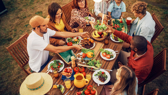 Friendly gathering of people sitting around an outdoor table with food and drinks