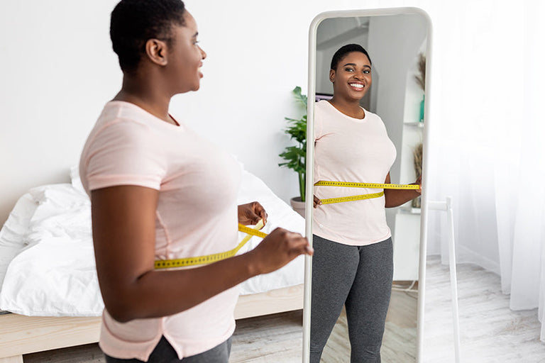 Smiling woman looking at herself in the mirror with a measuring tape around her waist