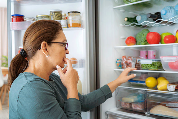 Woman standing at her fridge trying to decide what she should eat. 