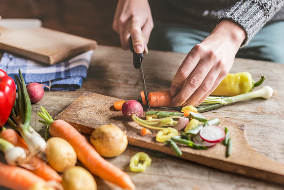 person chopping up a variety of vegetables on a cutting board.
