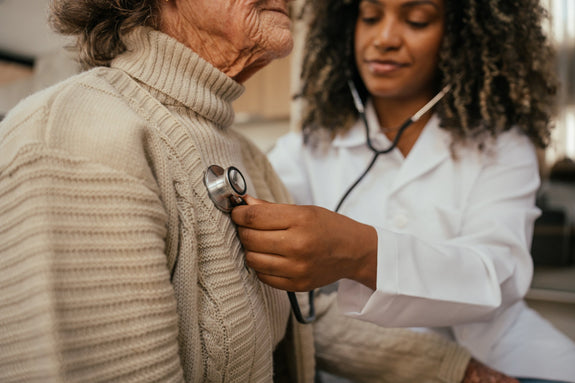 Healthcare professional listening to elderly woman's heart with stethoscope