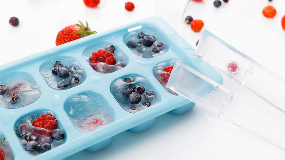 Ice cube tray filled with fruit ice cubes. The ice cubes have blueberries and raspberries in them. 