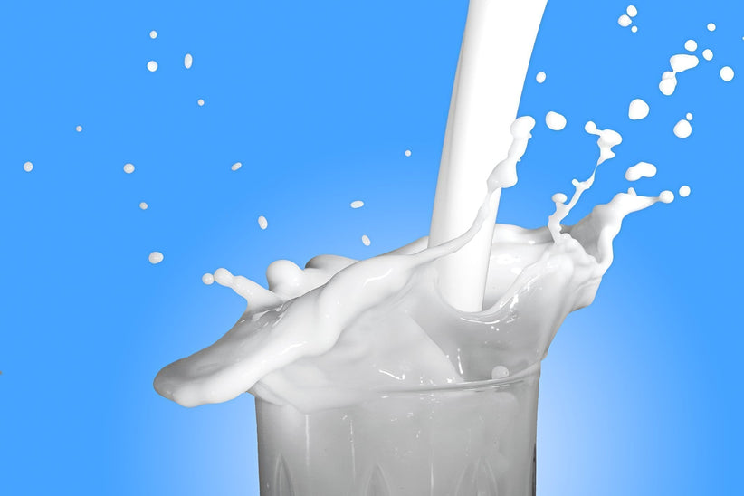 a glass of milk being poured against a bright blue background