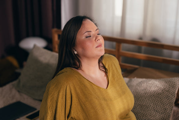 Woman sitting back relaxing, eyes closed, the sun shining on her face.